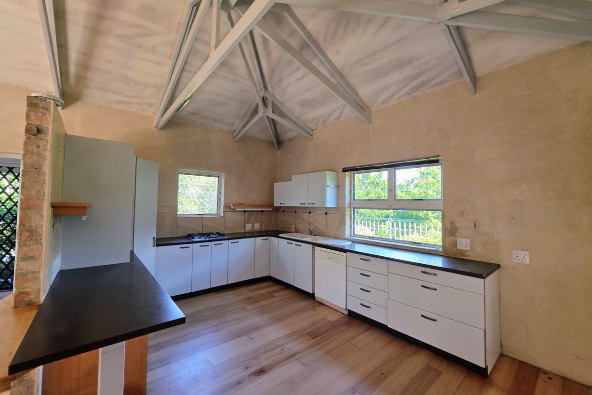 Spacious kitchen featuring vaulted ceilings with exposed trusses, white cabinetry, gas hob, and laminate flooring, offering a bright and functional layout.