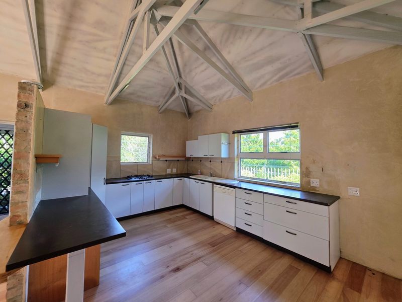 Spacious kitchen featuring vaulted ceilings with exposed trusses, white cabinetry, gas hob, and laminate flooring, offering a bright and functional layout.