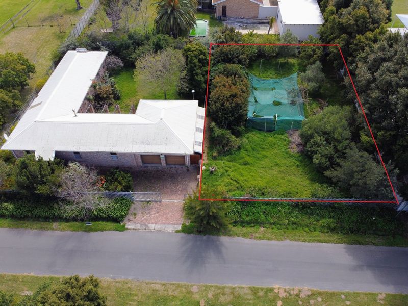 Aerial view of a residential property featuring a metal roof, paved driveway, and a large, partially overgrown garden area with perimeter fencing.
