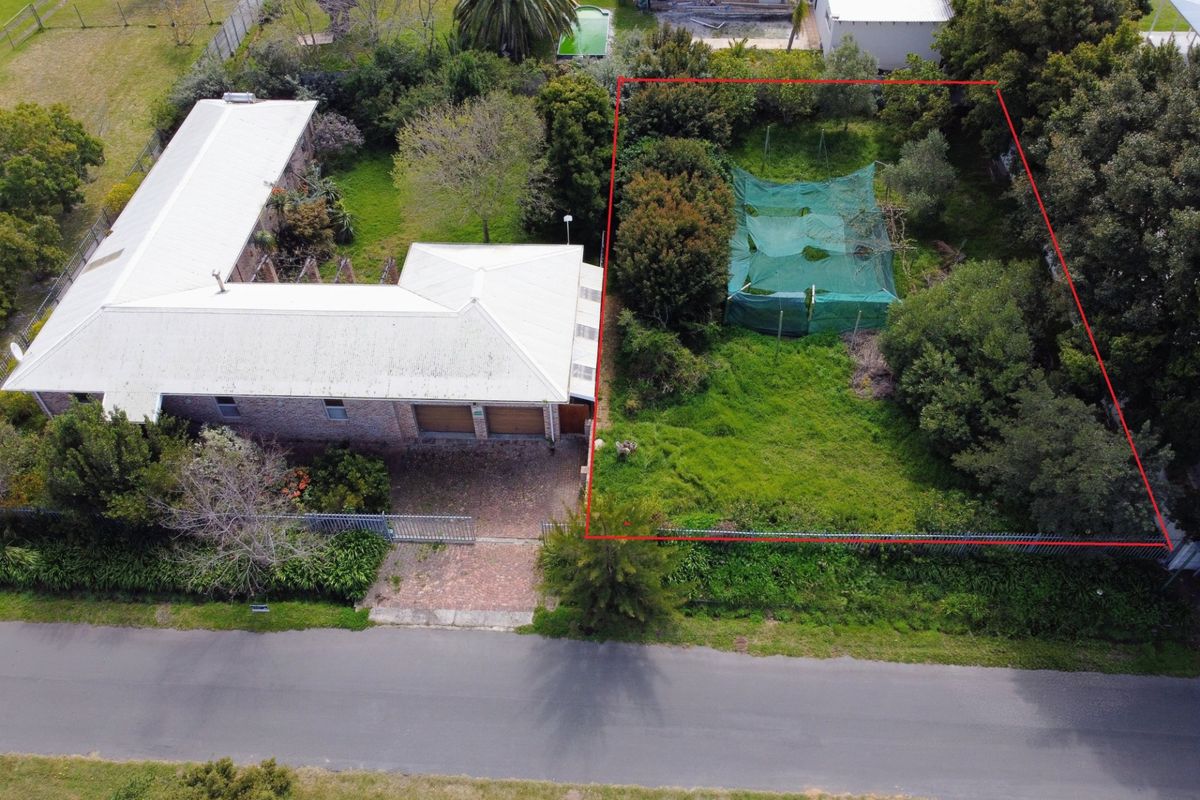 Aerial view of a residential property featuring a metal roof, paved driveway, and a large, partially overgrown garden area with perimeter fencing.