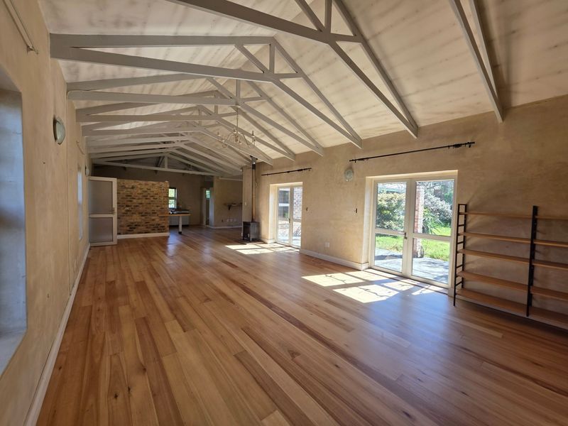 Spacious open-plan living area featuring vaulted ceilings with exposed trusses, hardwood flooring, a freestanding fireplace, and direct access to the garden through glass doors.