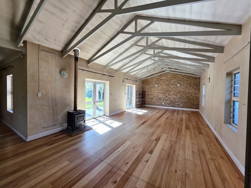 Spacious living area featuring vaulted ceilings with exposed trusses, a wood-burning fireplace, hardwood flooring, and a rustic exposed brick feature wall.