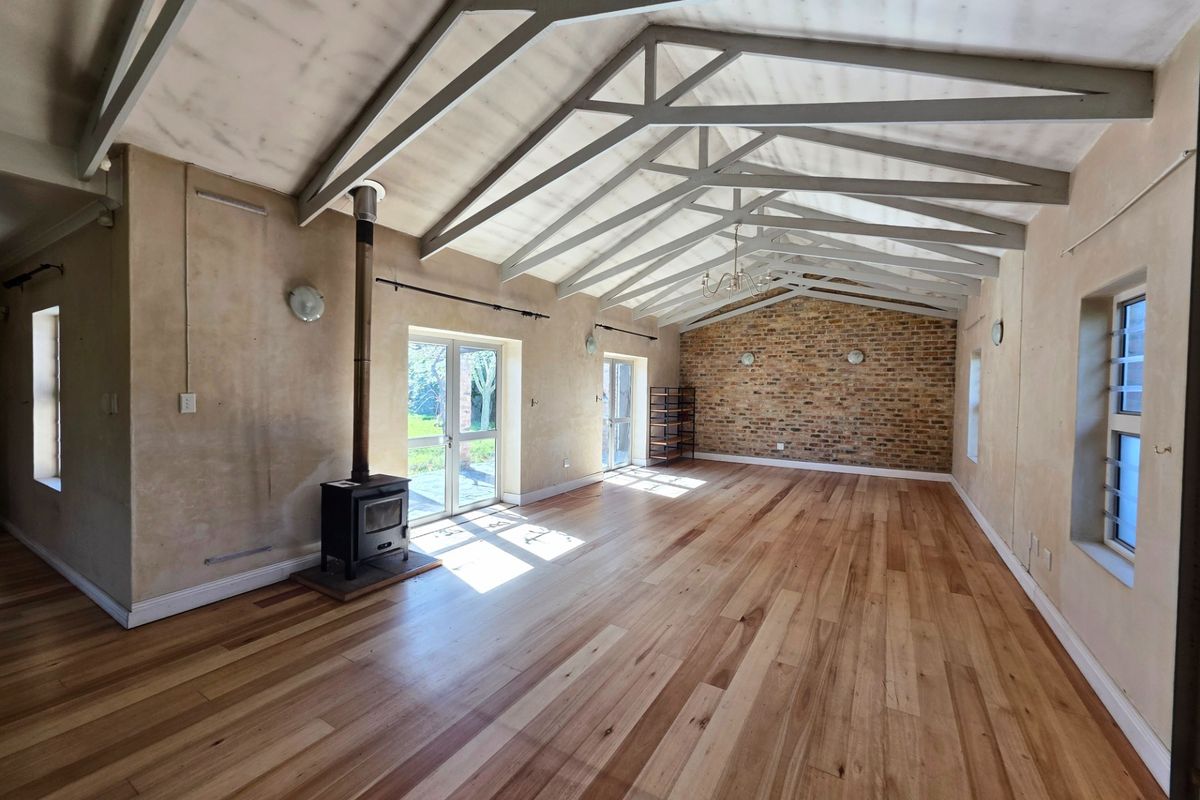 Spacious living area featuring vaulted ceilings with exposed trusses, a wood-burning fireplace, hardwood flooring, and a rustic exposed brick feature wall.
