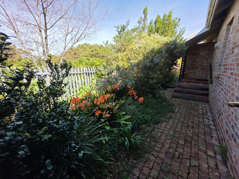 A rear garden area featuring brick paving, timber steps leading to the house, and established garden beds enclosed by metal fencing.