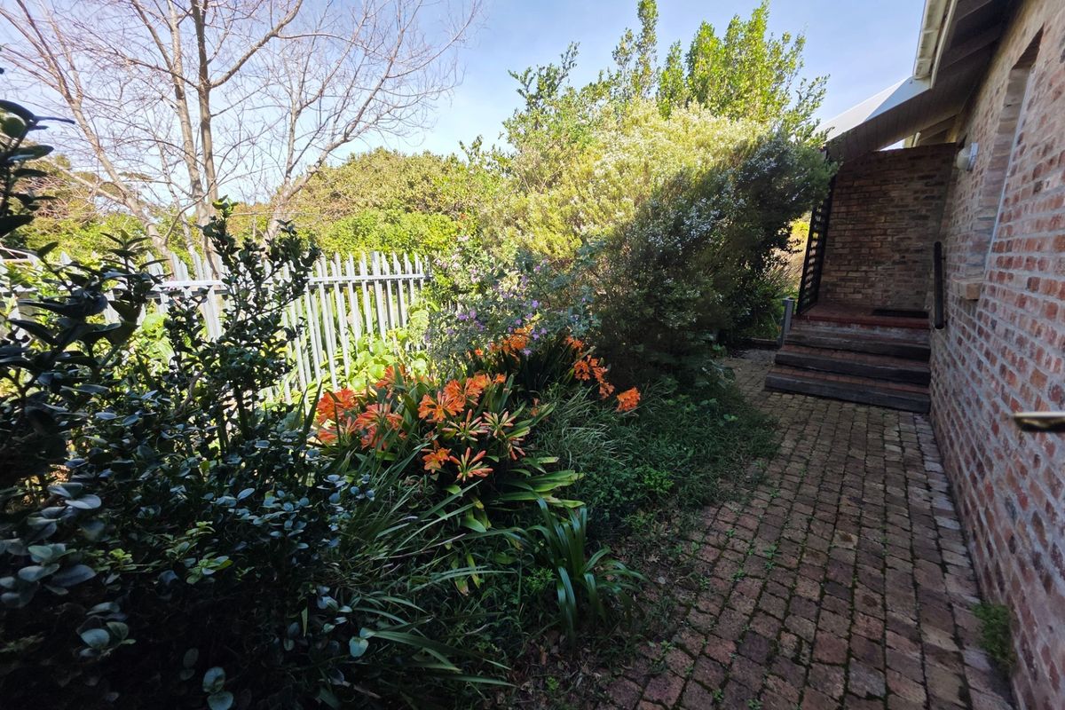 A rear garden area featuring brick paving, timber steps leading to the house, and established garden beds enclosed by metal fencing.
