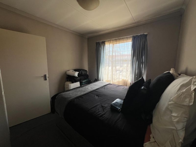 A standard bedroom featuring neutral wall tones, a window with security bars, and a functional layout suitable for a comfortable sleeping space.