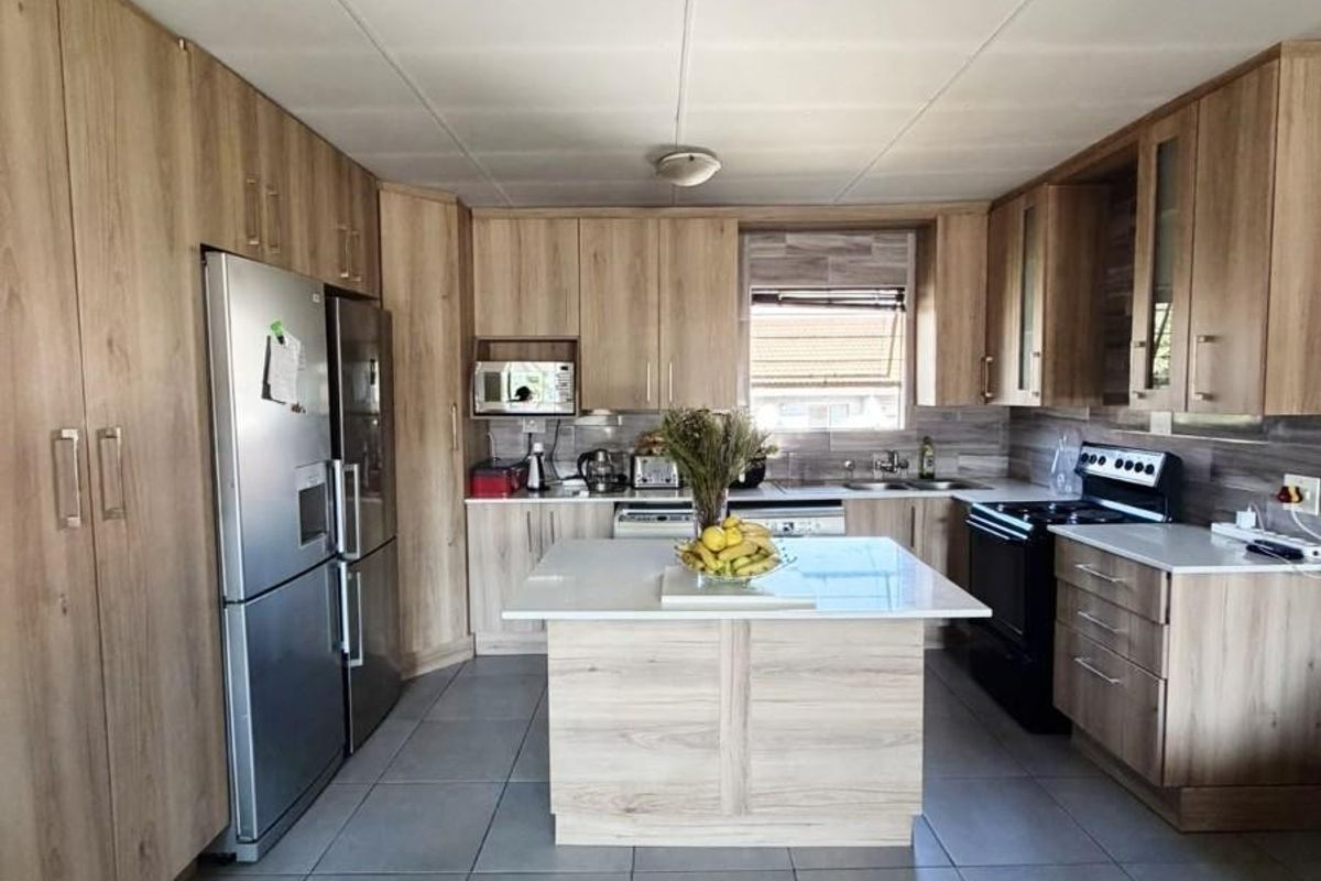A well-maintained kitchen featuring wood-finish cabinetry, a central island, tiled flooring, and integrated appliances, offering a functional and modern workspace.