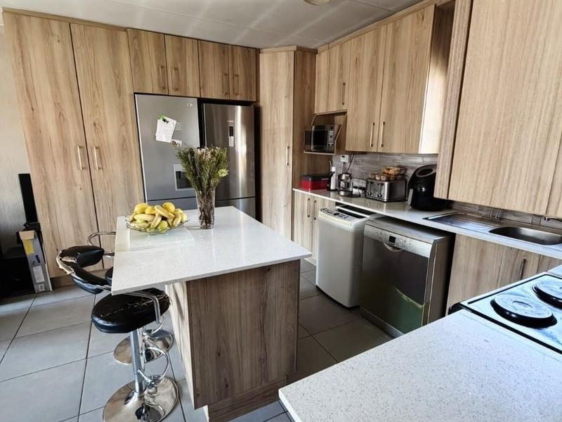 Modern kitchen featuring light wood-grain cabinetry, stone countertops, a central island, and tiled flooring, offering a functional and contemporary cooking space.