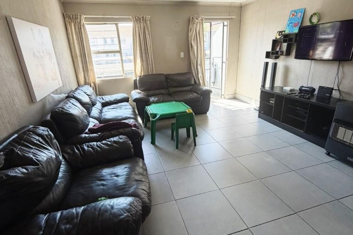 A living room featuring large floor tiles, neutral walls, and access to a balcony through a sliding glass door.