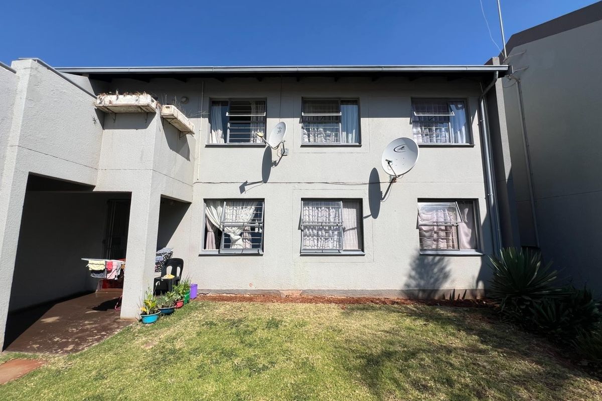 Rear view of the apartment building featuring a small private garden, concrete patio area, and multiple windows with security bars.