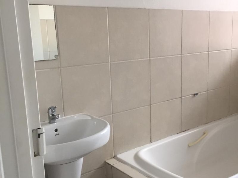 A compact bathroom featuring a pedestal basin, a built-in bathtub, and neutral wall tiling, requiring some maintenance and cosmetic updates.