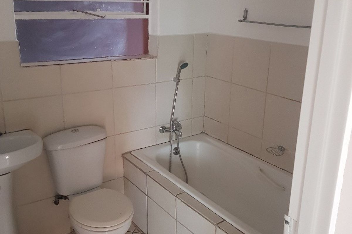 A functional bathroom featuring a pedestal basin, toilet, and bathtub with handheld shower mixer, finished with neutral wall and floor tiling.