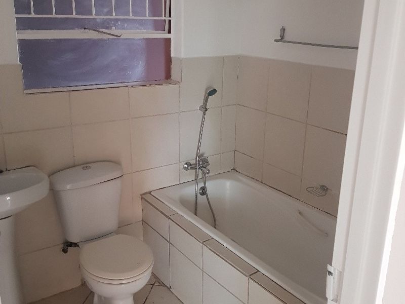 A functional bathroom featuring a pedestal basin, toilet, and bathtub with handheld shower mixer, finished with neutral wall and floor tiling.