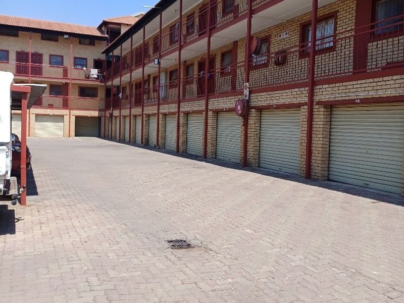 Exterior view of an apartment complex featuring a paved driveway, multiple metal roller garage doors, and multi-level balcony access with brick facade finishes.