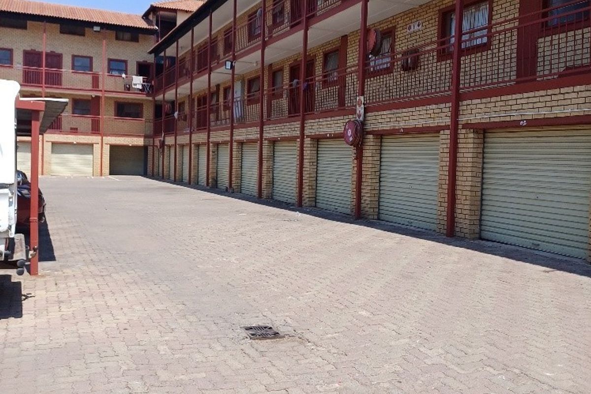Exterior view of an apartment complex featuring a paved driveway, multiple metal roller garage doors, and multi-level balcony access with brick facade finishes.