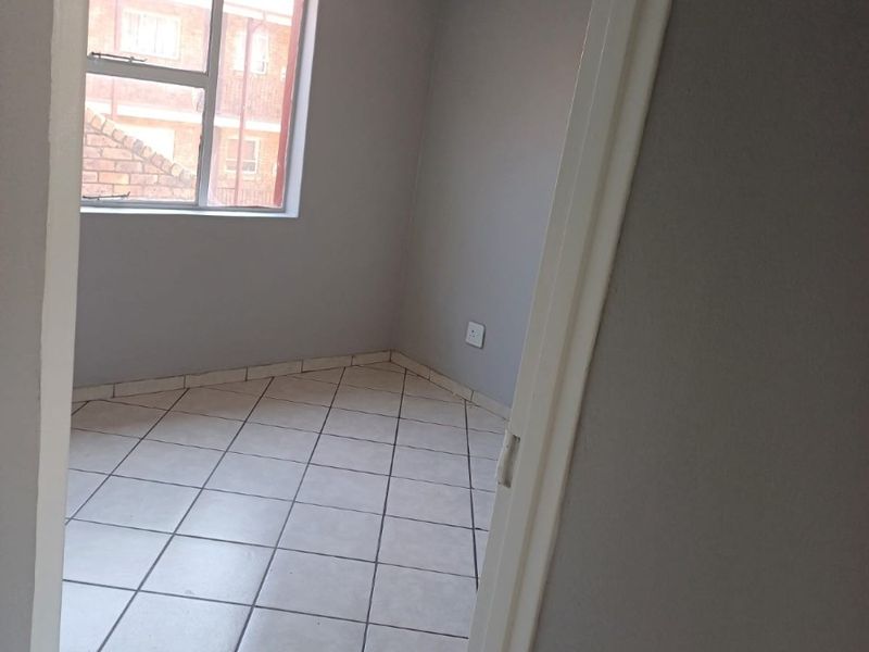 An empty bedroom featuring neutral grey walls, tiled flooring, and a large window allowing for natural light.