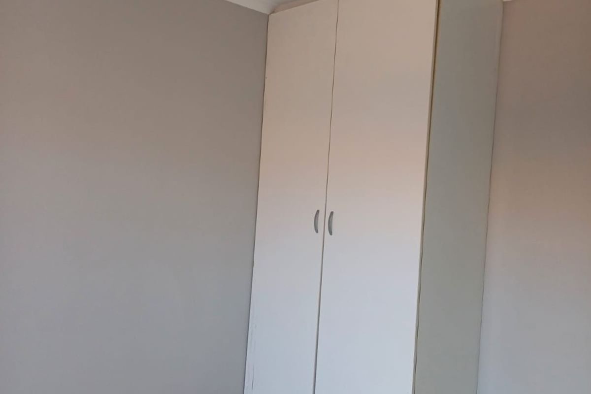 A simple, empty bedroom featuring neutral wall paint, tiled flooring, and a functional built-in wardrobe.