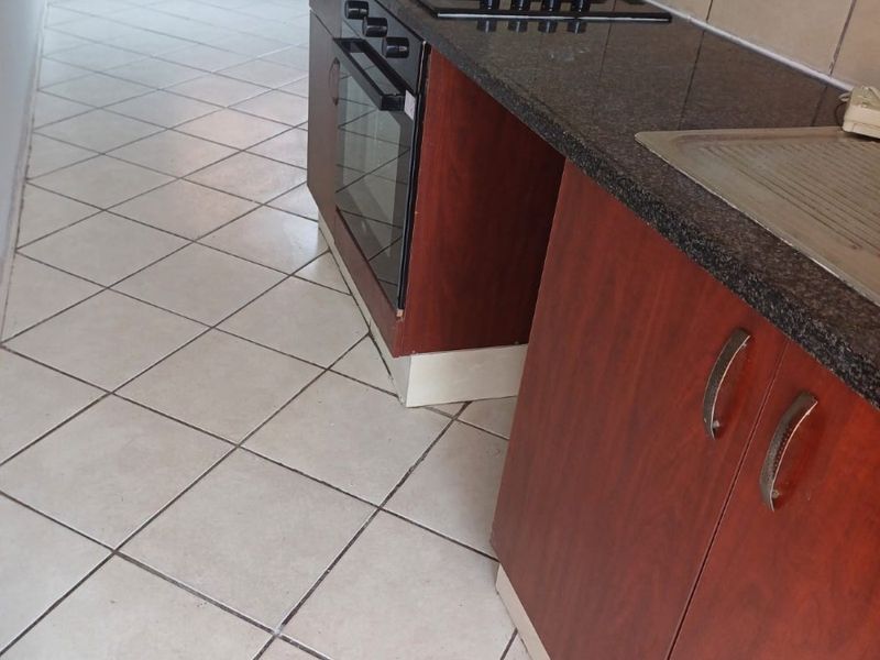 A functional kitchen featuring dark wood cabinetry, granite countertops, a built-in oven and hob, and tiled flooring throughout.
