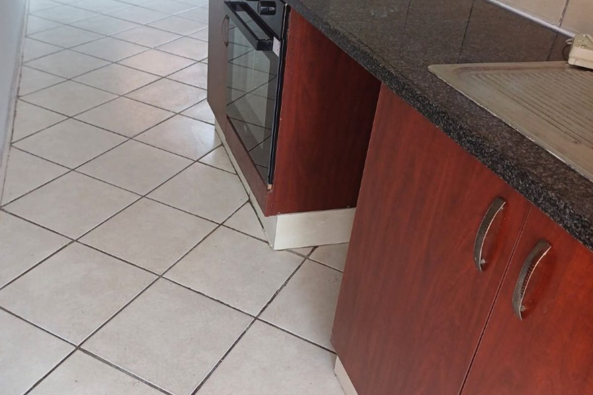 A functional kitchen featuring dark wood cabinetry, granite countertops, a built-in oven and hob, and tiled flooring throughout.