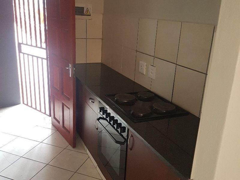 Compact kitchen featuring built-in oven, electric hob, granite countertops, and tiled backsplash, with direct access to an exterior security gate.