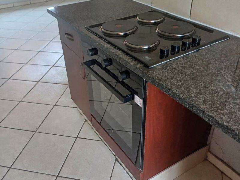A functional kitchen area featuring a built-in oven, electric hob, granite countertops, and tiled flooring throughout.