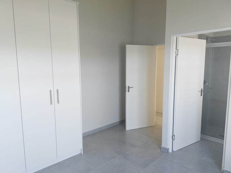 A clean, modern bedroom featuring neutral tiled flooring, built-in cupboards, and direct access to an en-suite bathroom.