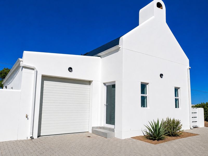 A modern, well-maintained white exterior facade featuring a single garage, paved driveway, and a prominent chimney against a clear blue sky.