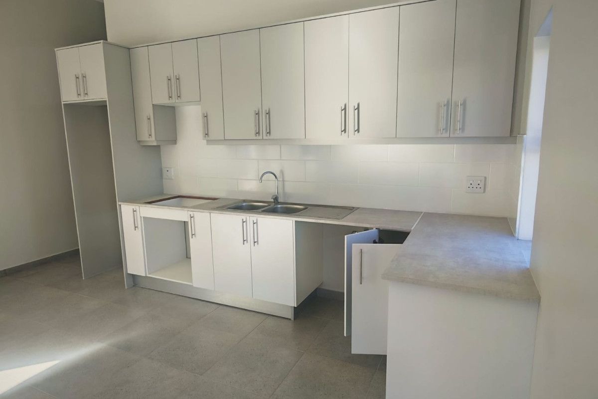 A clean, modern kitchen featuring white built-in cabinetry, grey laminate countertops, a stainless steel sink, and neutral tiled flooring.