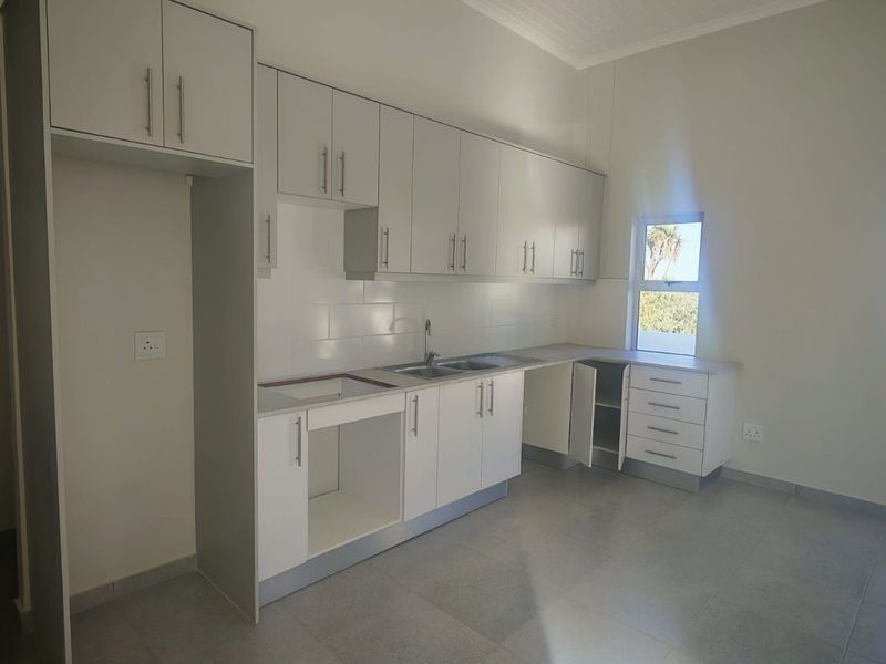 A clean, modern kitchen featuring white cabinetry, tiled flooring, and a neutral backsplash, ready for appliance installation.