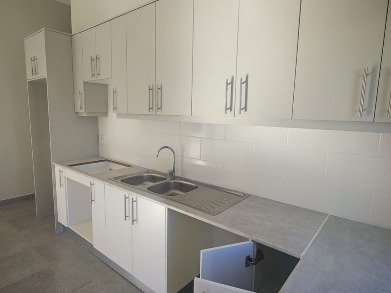 A modern, empty kitchen featuring white cabinetry, grey laminate countertops, a stainless steel double sink, and a clean subway tile backsplash.