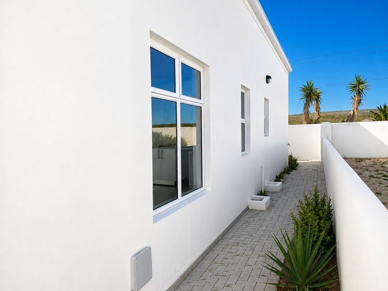 A clean, well-maintained rear exterior view featuring a paved walkway, white rendered walls, and modern casement windows.