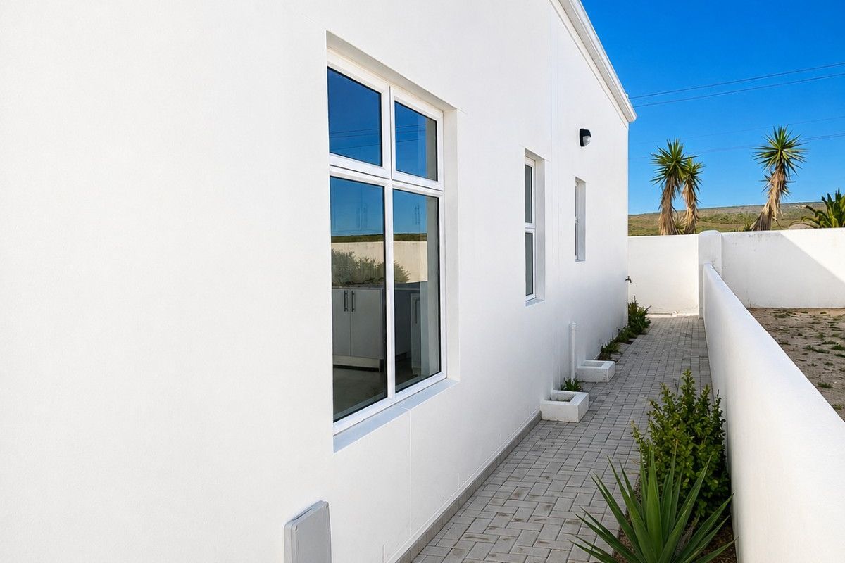 A clean, well-maintained rear exterior view featuring a paved walkway, white rendered walls, and modern casement windows.