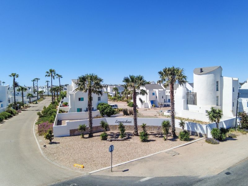 Aerial view of the Lampiesbaai residential estate entrance, featuring white architectural facades, landscaped gardens, and paved access roads under a clear blue sky.