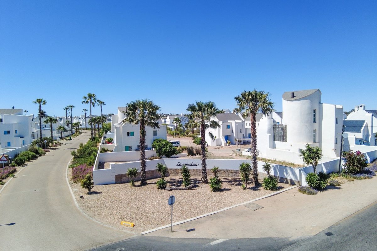 Aerial view of the Lampiesbaai residential estate entrance, featuring white architectural facades, landscaped gardens, and paved access roads under a clear blue sky.