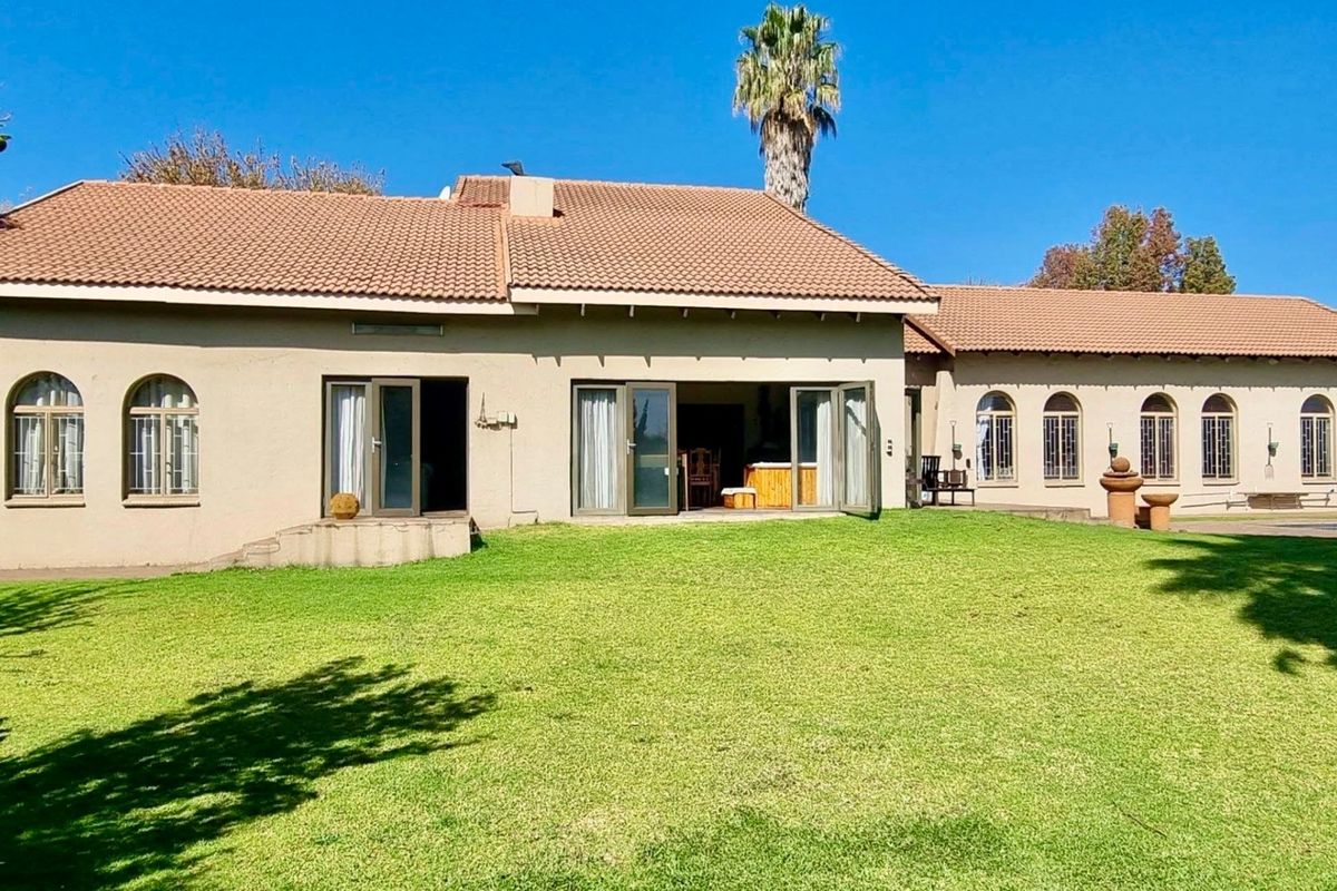 Rear view of the house featuring a large lawn, tiled roof, and multiple arched windows with bi-fold doors leading to the interior.