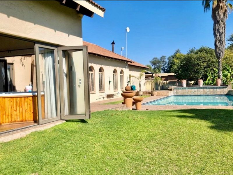 Rear exterior view featuring a swimming pool, landscaped lawn, tiled patio area, and bi-fold doors leading into the home.