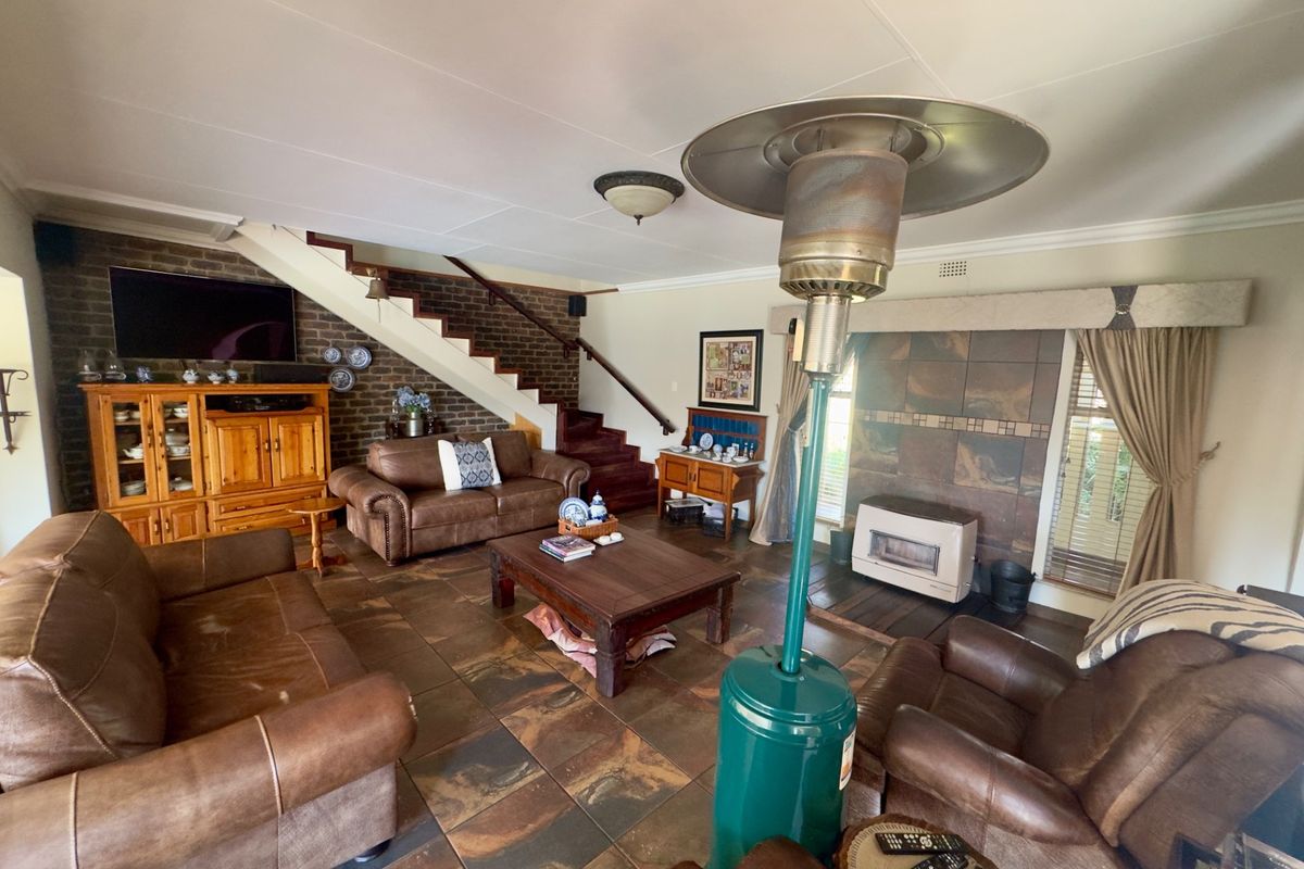 Spacious living room featuring a brick accent wall, staircase, tiled flooring, and a built-in fireplace, offering a warm and traditional atmosphere.