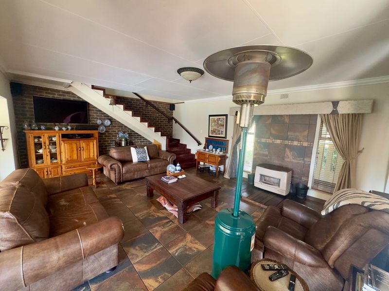 Spacious living room featuring a brick accent wall, staircase, tiled flooring, and a built-in fireplace, offering a warm and traditional atmosphere.