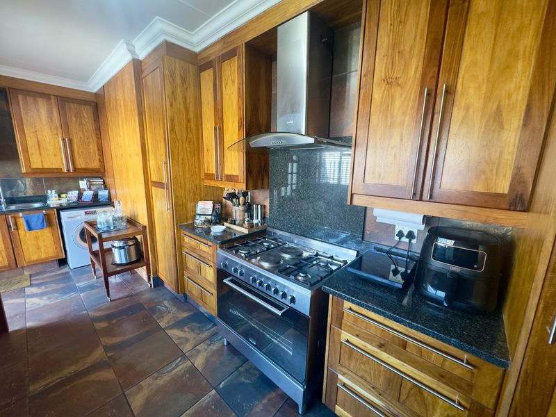 A functional kitchen featuring warm-toned wooden cabinetry, granite countertops, stone tile flooring, and a stainless steel gas stove with an integrated extractor fan.