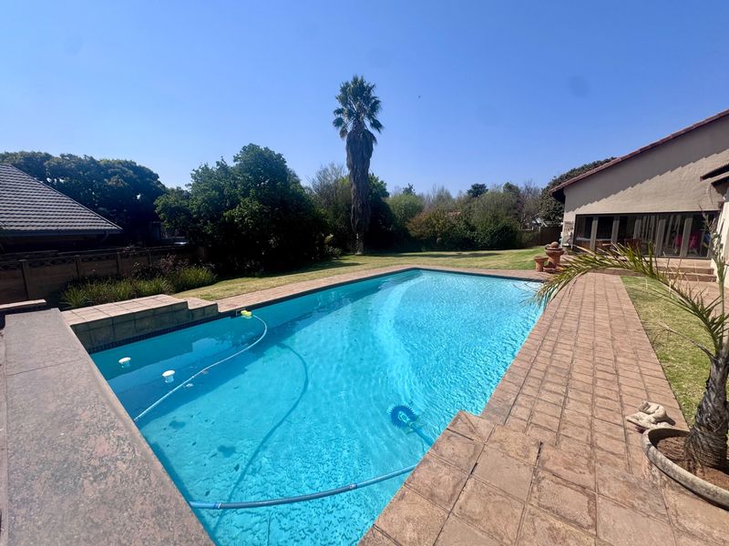 A well-maintained swimming pool area featuring a paved deck, surrounding lawn, and established garden, providing a pleasant outdoor entertainment space.
