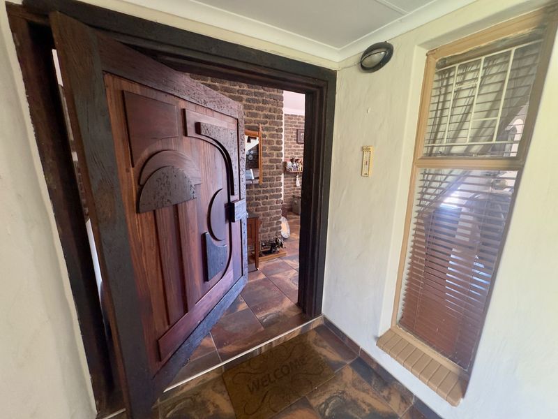 Entrance area featuring a unique carved solid wood door, tiled flooring, and a rustic brick feature wall leading into the main living space.