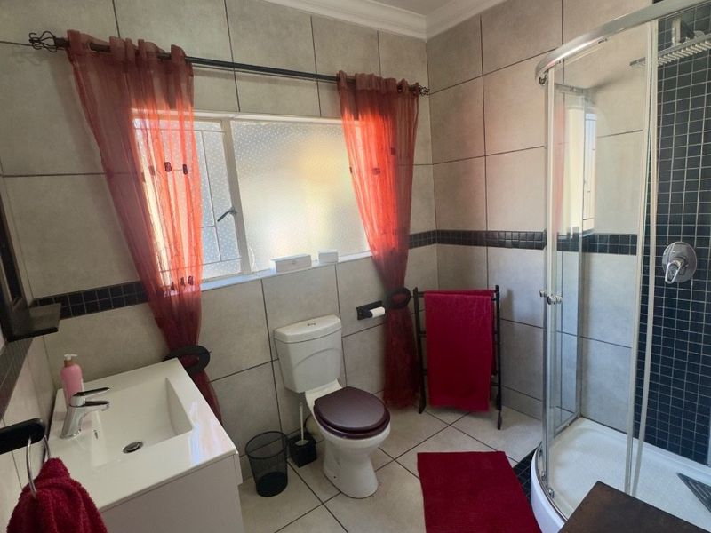 A functional bathroom featuring a corner shower enclosure, vanity basin, and toilet with neutral wall and floor tiling.