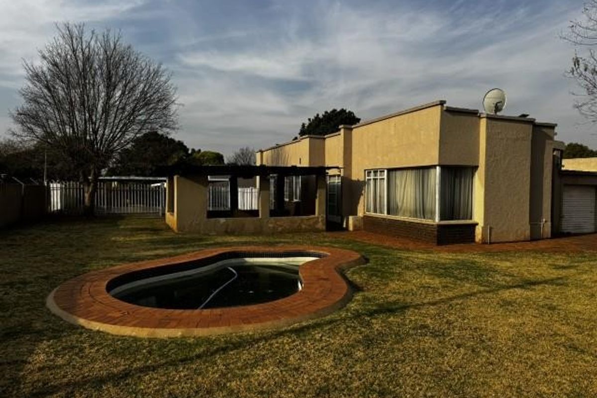 Rear view of the property featuring a swimming pool with brick coping, a covered patio area, and a detached garage.