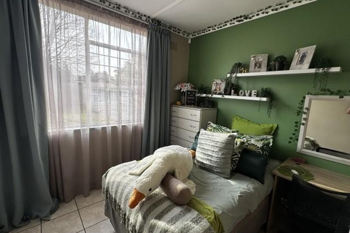 A cozy bedroom featuring tiled flooring, a large window with curtains, and built-in wall shelving against a green accent wall.