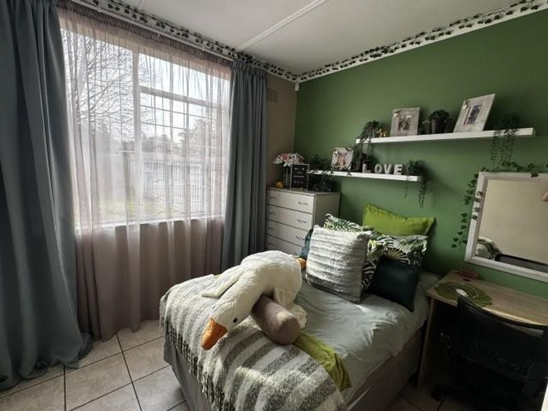 A cozy bedroom featuring tiled flooring, a large window with curtains, and built-in wall shelving against a green accent wall.