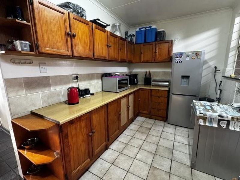 A functional kitchen featuring traditional wooden cabinetry, tiled backsplash, and tiled flooring, offering a dated aesthetic with potential for modern renovation.