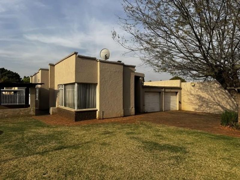 Front view of a residential property featuring a double garage, paved driveway, and established lawn area.