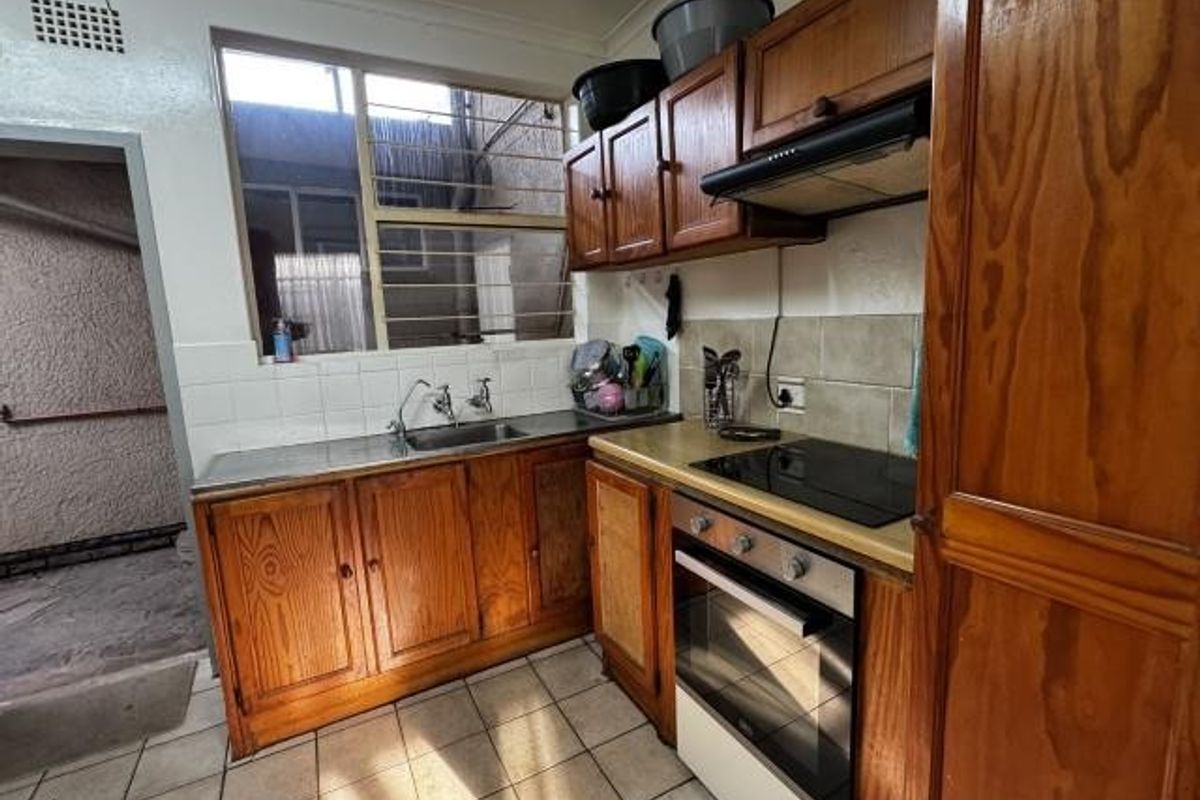 A functional kitchen featuring wooden cabinetry, built-in oven, electric hob, and tiled splashbacks, offering a dated aesthetic ready for modernization.