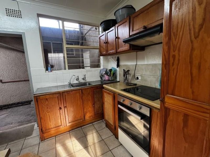 A functional kitchen featuring wooden cabinetry, built-in oven, electric hob, and tiled splashbacks, offering a dated aesthetic ready for modernization.