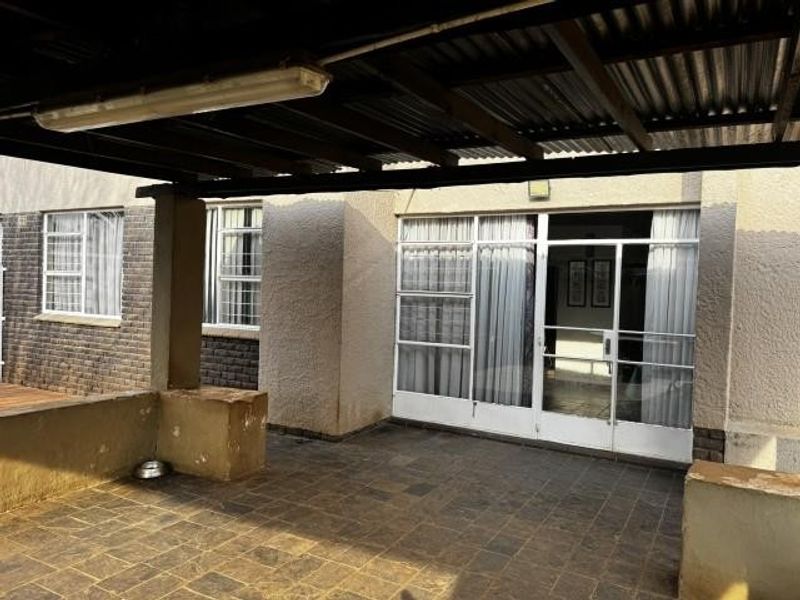 A covered patio area featuring tiled flooring, a corrugated metal roof, and sliding glass door access to the interior living space.